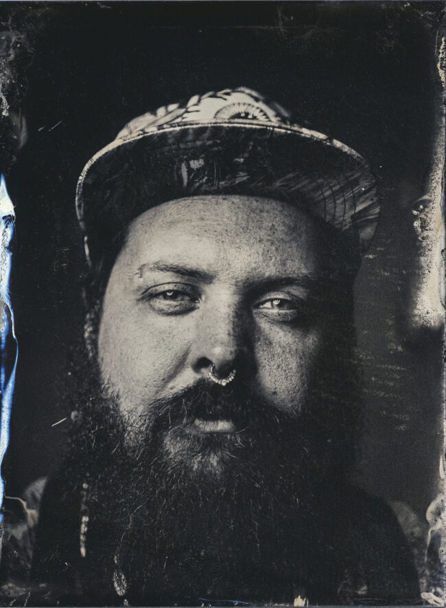 Nassplatte, Schwarz-Weiß, Portraitaufnahme von jungen Mann mir Basecap, Sommersprossen, Vollbart und Nasenring