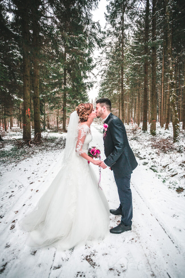 Hochzeit, Portrait, Paar steht im verschneiten Wald und küsst sich