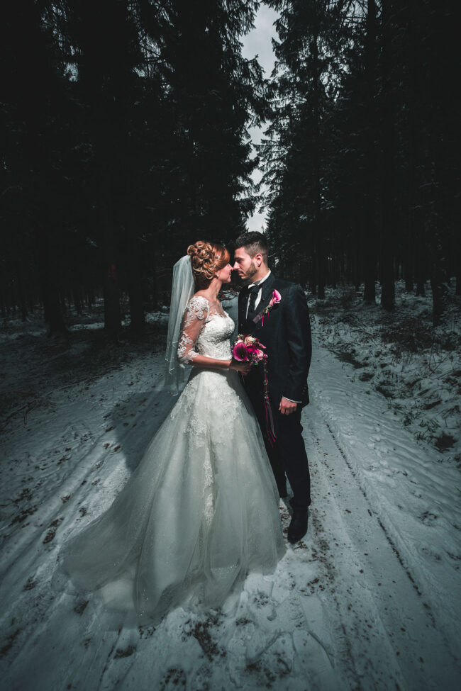 Hochzeit, Portrait, Paar steht im verschneiten Wald bei Dämmerung und schaut sich an