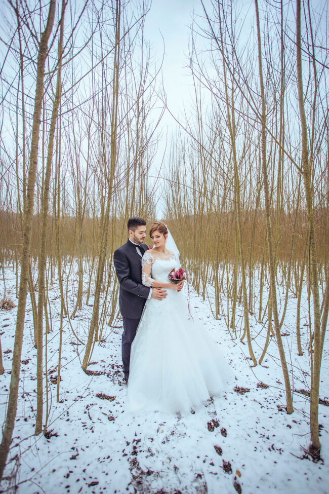 Hochzeit, Braut steht mit dem Rücken an Bräutigam gelehnt in einer verschneiten Wandschonung