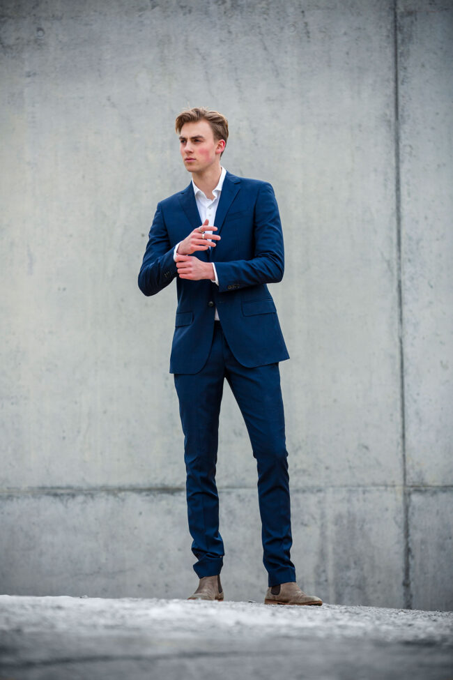 Portrait, junger Mann in blauem Anzug steht vor Betonwand, Ganzaufnahme