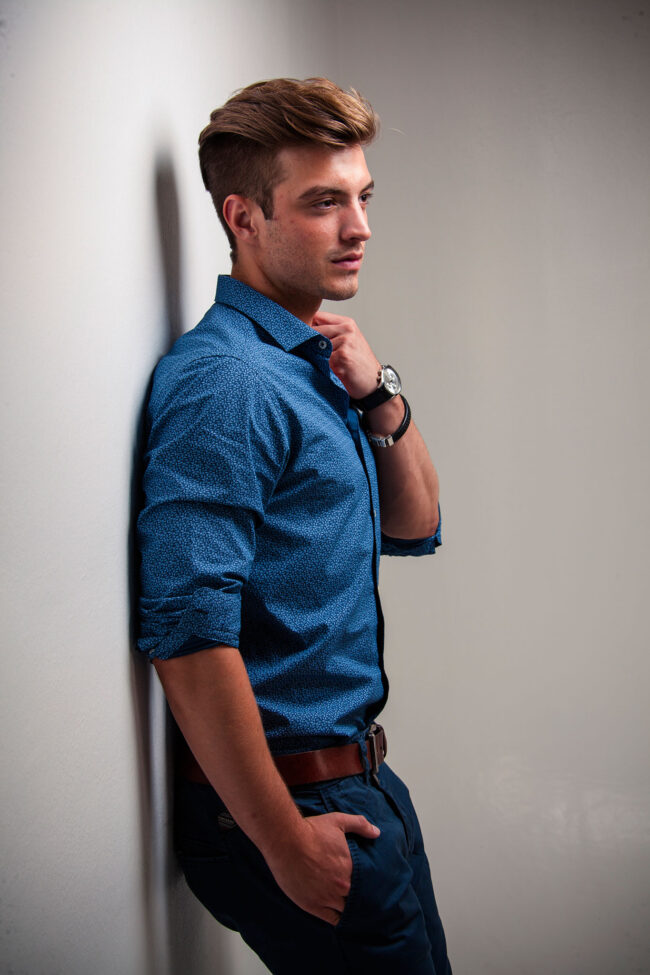 Portrait, Mann in Hemd und Jeans steht an die Wand gelehnt und schaut aus dem Bild, Halbaufnahme