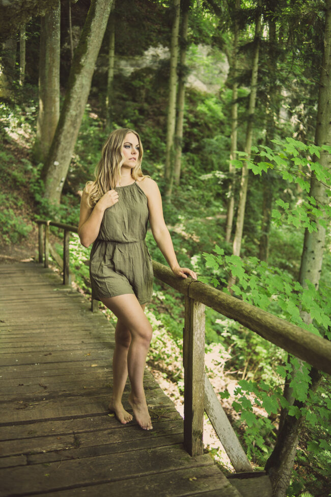 Portrait, Frau steht auf Holzbrücke im grünen Wald und schaut in die Ferne, Ganzaufnahme