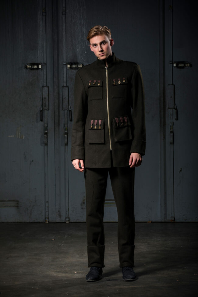 Fashion, Mode,junger Mann mit dunkelgrünem Anzug. Auf der Jacke sind goldenen Orden ähnliche Verzierungen und ein Reisverschluss, Ganzaufnahme