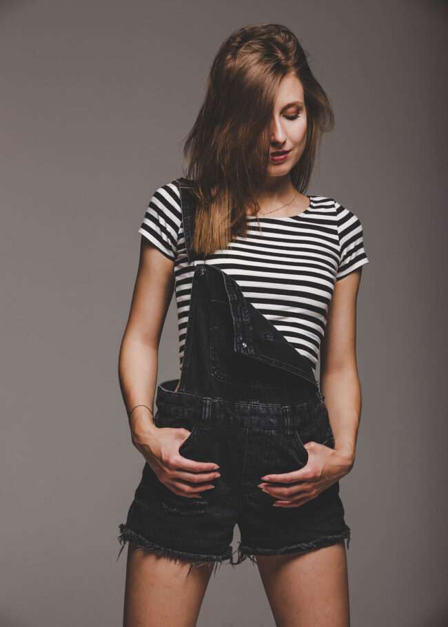 Portrait, Frau in kurzer Latzhose und gestreiftem Oberteil, grauer Hintergrund, Halbnahaufnahme