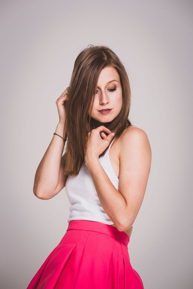 Portrait, Frau mit linkem Rock und weißem Top, schaut nach rechts unten, grauer Hintergrund
