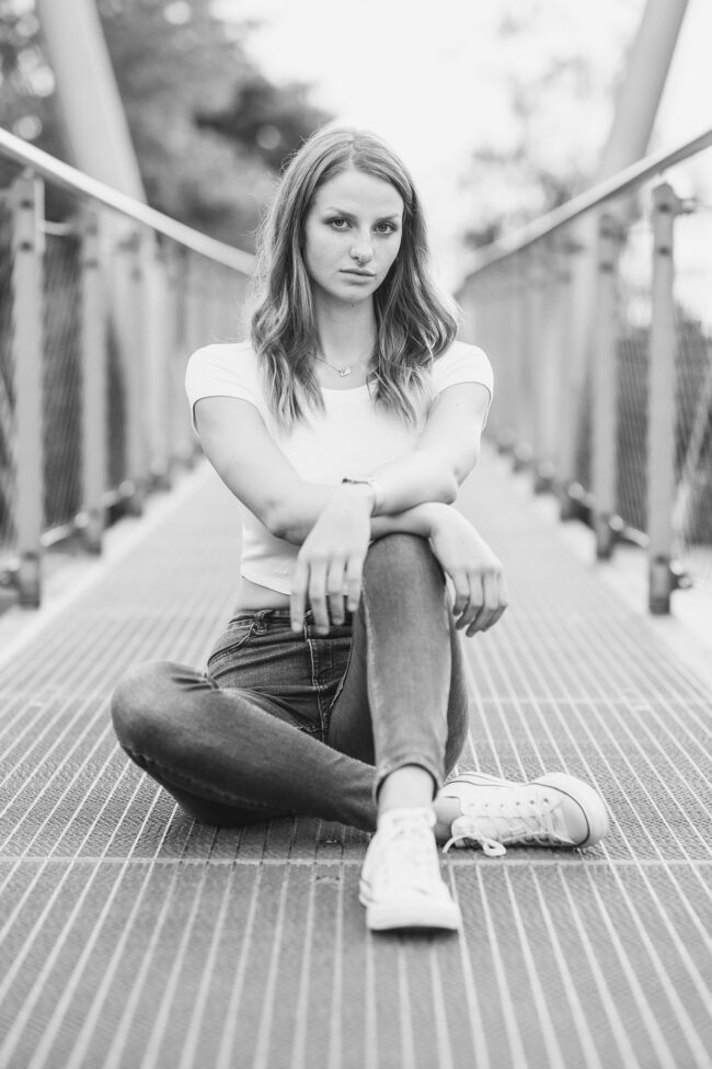 Portrait, Frau in Jeans und T-Shirt sitzt auf Brücke, Ganzaufnahme, Schwarz-Weiß