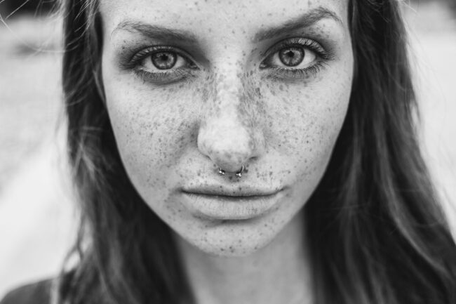 Portrait, Nahaufnahme Frau mit Nasenpiercing, ernster Blick in Kamera, Schwarz-Weiß