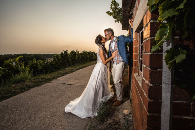 Hochzeit, Brautpaar steht küssend an einem Wengerthäuschen in der Abendsonne