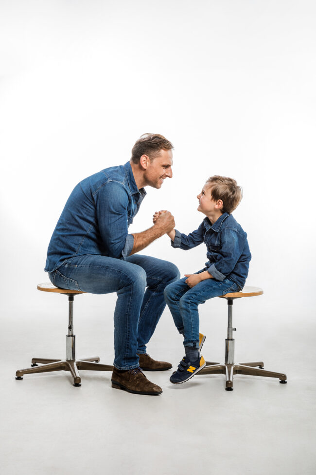 Familie, Vater und Sohn sitzen sich gegenüber und schlagen ein und lachen sich an