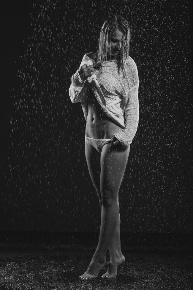 Sensual, Frau mit Pulli und Höschen auf Zehenspitzen stehend, von Wassertropfen beregnet, Schwarz-weiß
