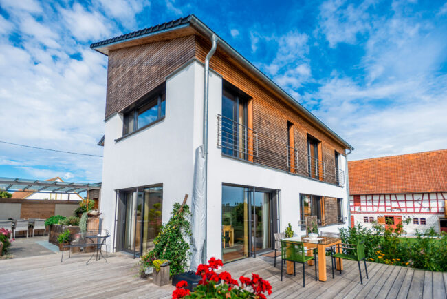 Architektur, modernes, schmales Einfamilienhaus, mit Teilholzverkleidung des oberen Stockwerks, Holzterrasse und Garten