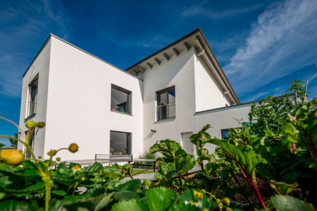 Architektur, Wohnhaus mit weißer Fassade, hintere Ansicht aus Garten, vor blauem Himmel