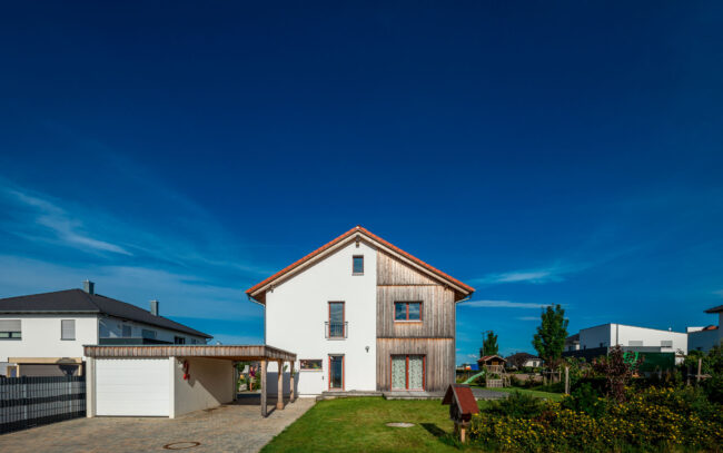 Architektur, Wohnhaus mit weißer Fassade und Holz mit grünem Garten vor blauem Himmel, Frontansicht