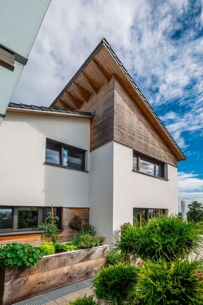 Architektur, Aufnahme weißes Haus mit Holzgiebel, davor steht ein Hochbeet mit Gemüse