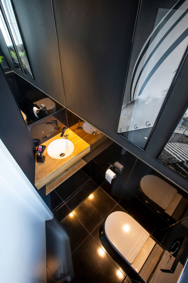 Interieur Badezimmer, Toilette mit kleinem Waschbecken mit Holztisch und hohen Spiegeln, schwarze Bodenfliesen, Ansicht von oben