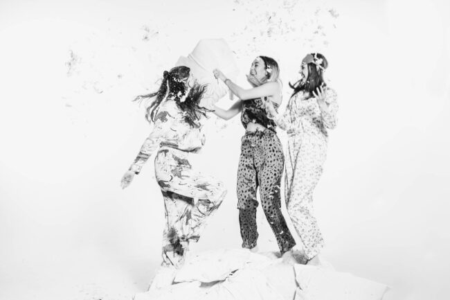 Freundschaftsshooting, drei Frauen im Pyjama lachen in die Kamera und machen eine Kissenschlacht, Schwarz-Weiß