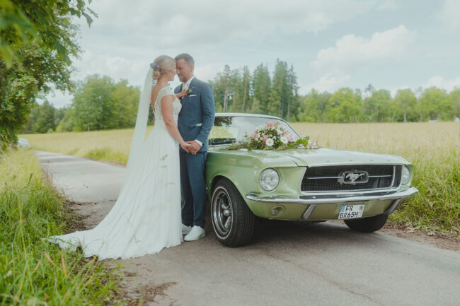 Hochzeit, Brautpaar lehnt sich an einen Oldtimer und schaut sich gegenseitig an, Ganzkörperaufnahme, Querformat