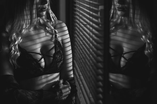 Sensual, Frau steht vor Fenster mit Jalousien, Nahaufnahme mit angeschnittenem Gesicht, Schwarz-Weiß