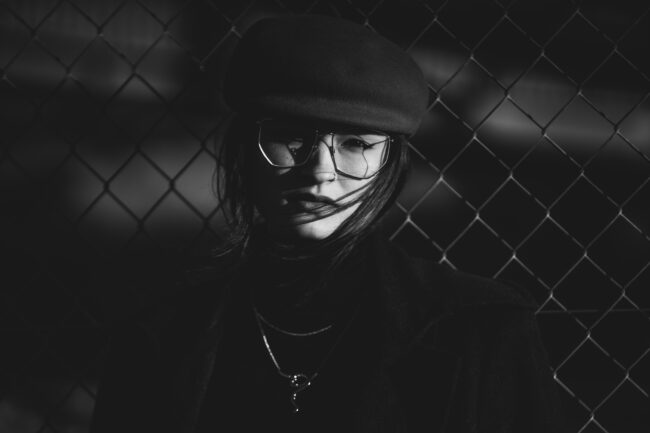 Portrait, Nahaufnahme, junge Frau mit Brille und Hut vor Gitterzaun, Schwarz Weiß