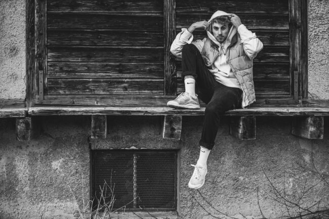 Portrait, Junger Mann auf Holzbrett sitzend, Ganzaufnahme, Schwarz Weiß