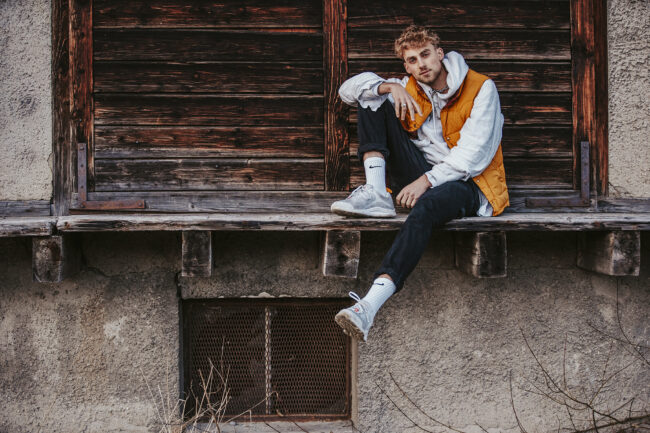 Portrait, Junger Mann auf Holzbrett sitzend, Ganzaufnahme