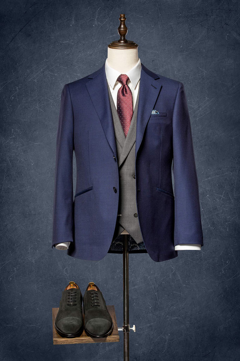 Anzug an einer Schneiderpuppe, daneben liegen die passenden Schuhe.