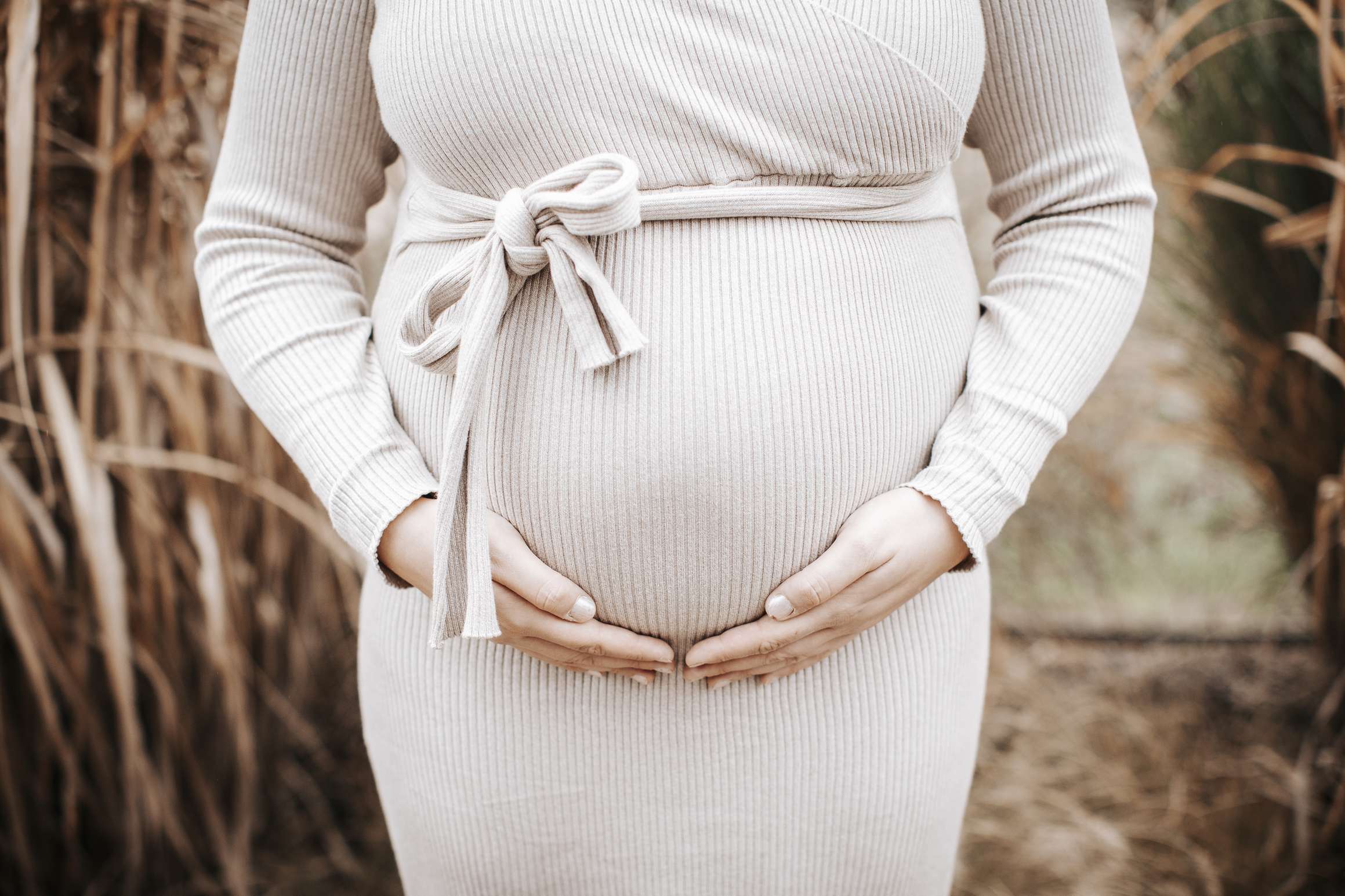 Schwangere frau in beigem kleid haelt ihren babybauch im freien