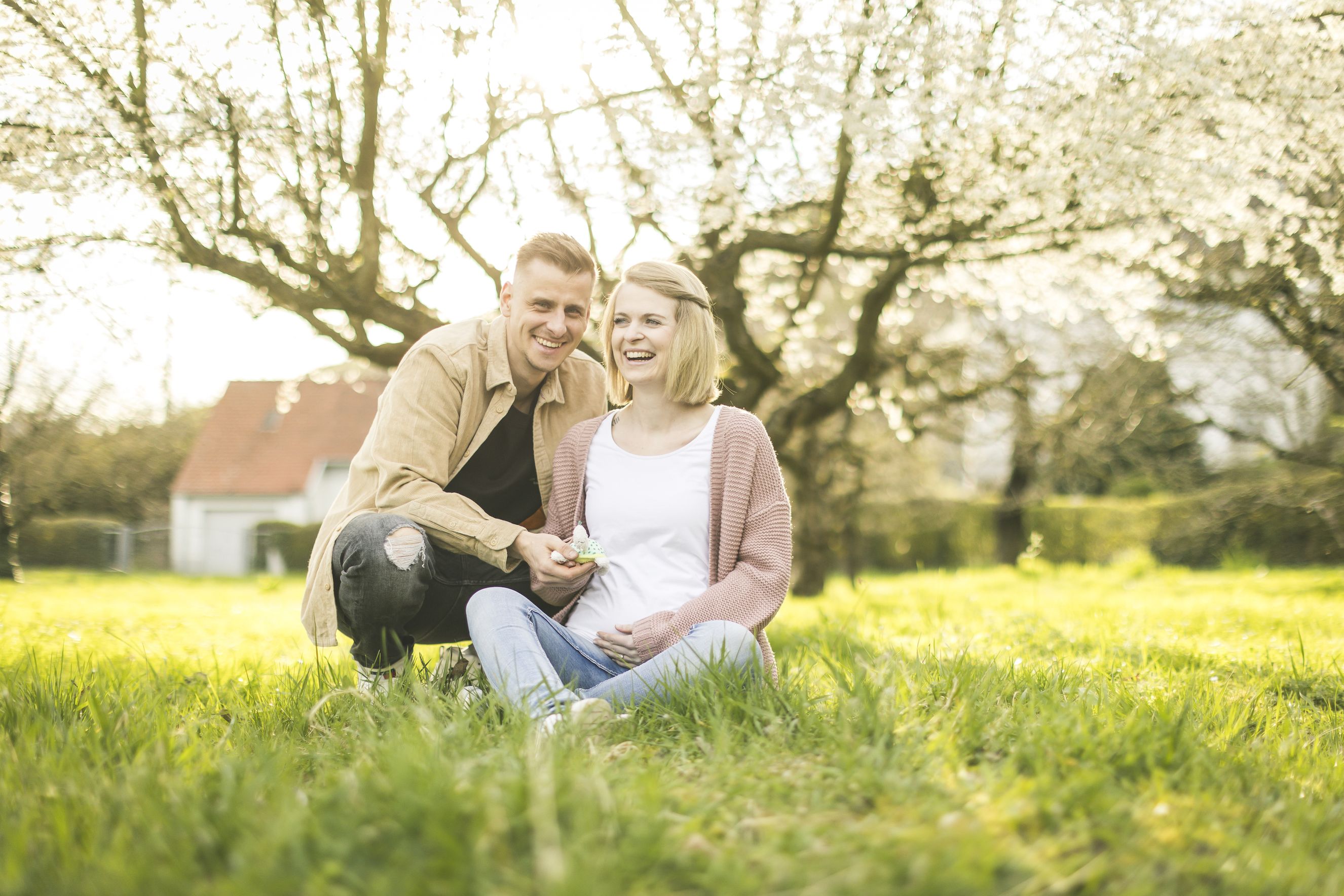 Ein paar sitzt in einer bluehenden fruehlingswiese und freut sich auf ihr baby.