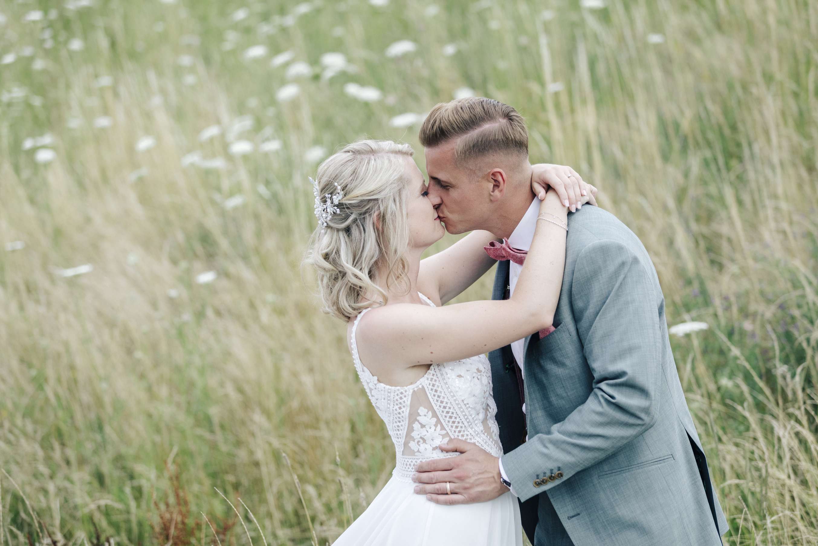 Brautpaar kuesst sich in einer wiese waehrend eines fotoshootings.