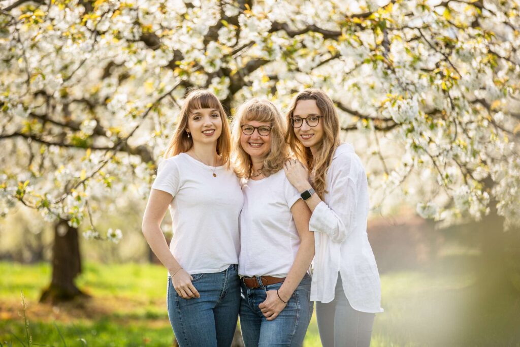 Drei frauen posieren laechelnd unter bluehenden baeumen im fruehling.