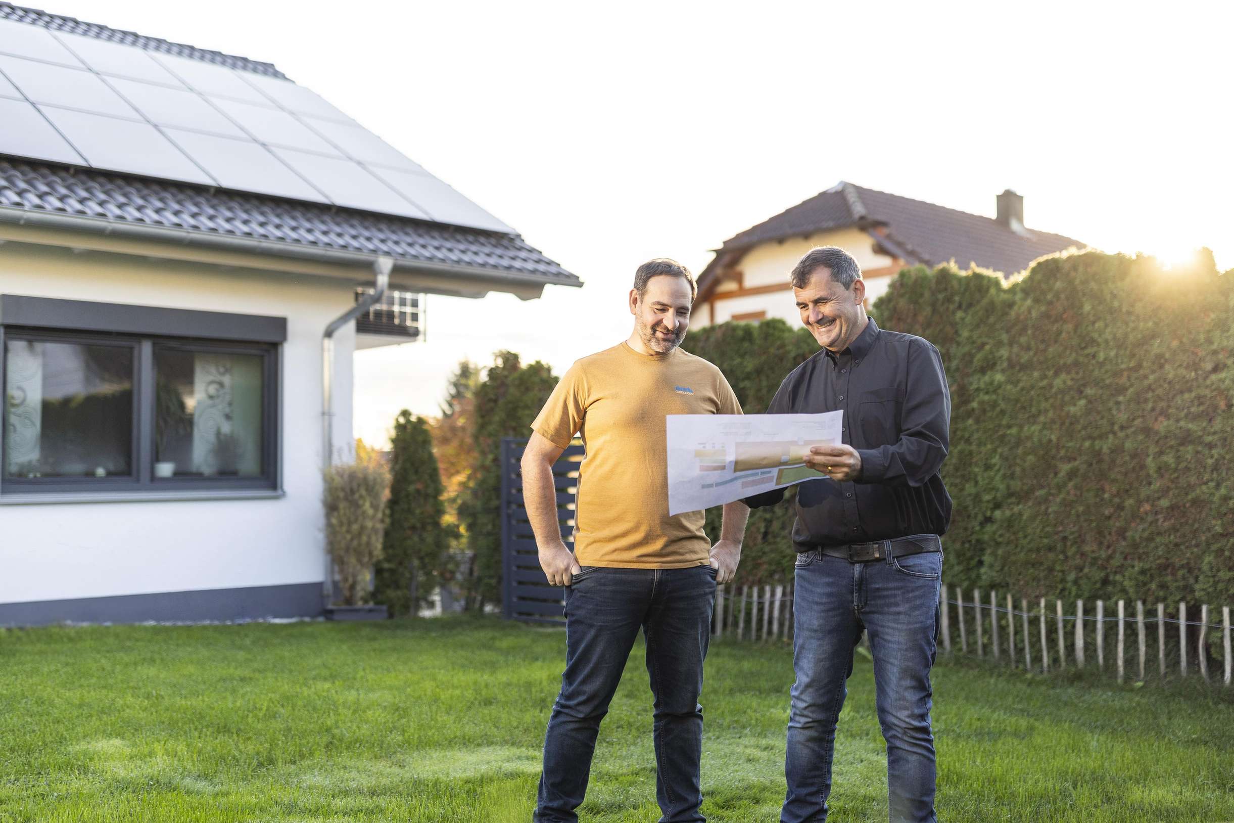 Zwei Personen planen eine Photovoltaik-Installation vor einem Haus.