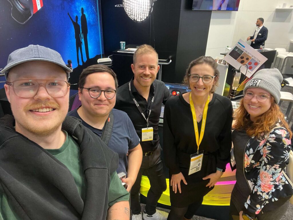 Eine Gruppe von fuenf Personen posiert fuer ein Foto in einem Innenraum.