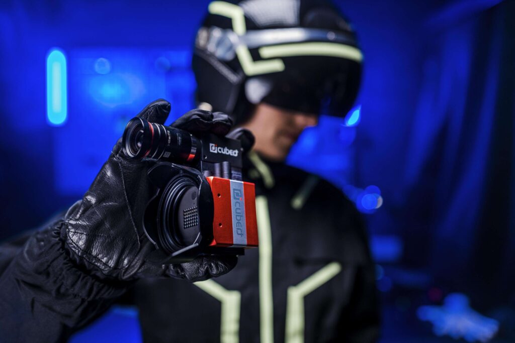 Person mit VR-Headset haelt Hyperspektralkamera in dunkler Umgebung.