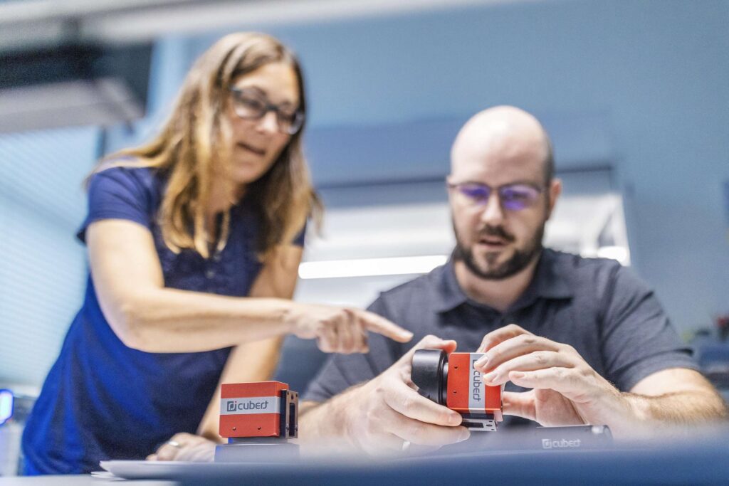 Zwei Mitarbeiter von Cubert betrachten eine Hyperspektralkamera.