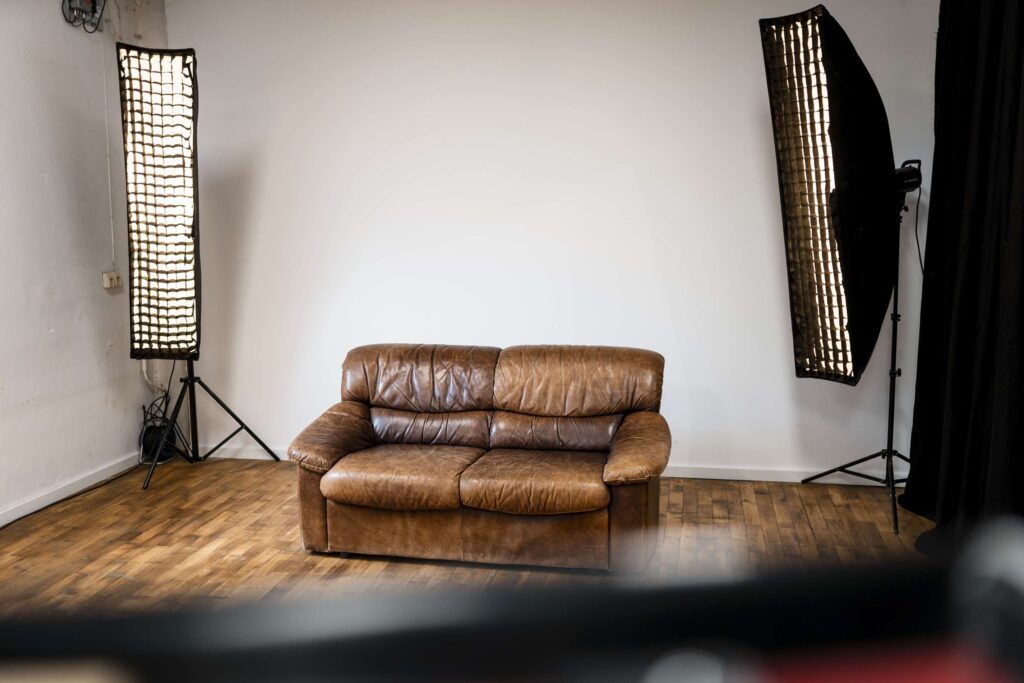 Ein Fotostudio-Setup mit braunem Ledersofa und Beleuchtungsausruestung.