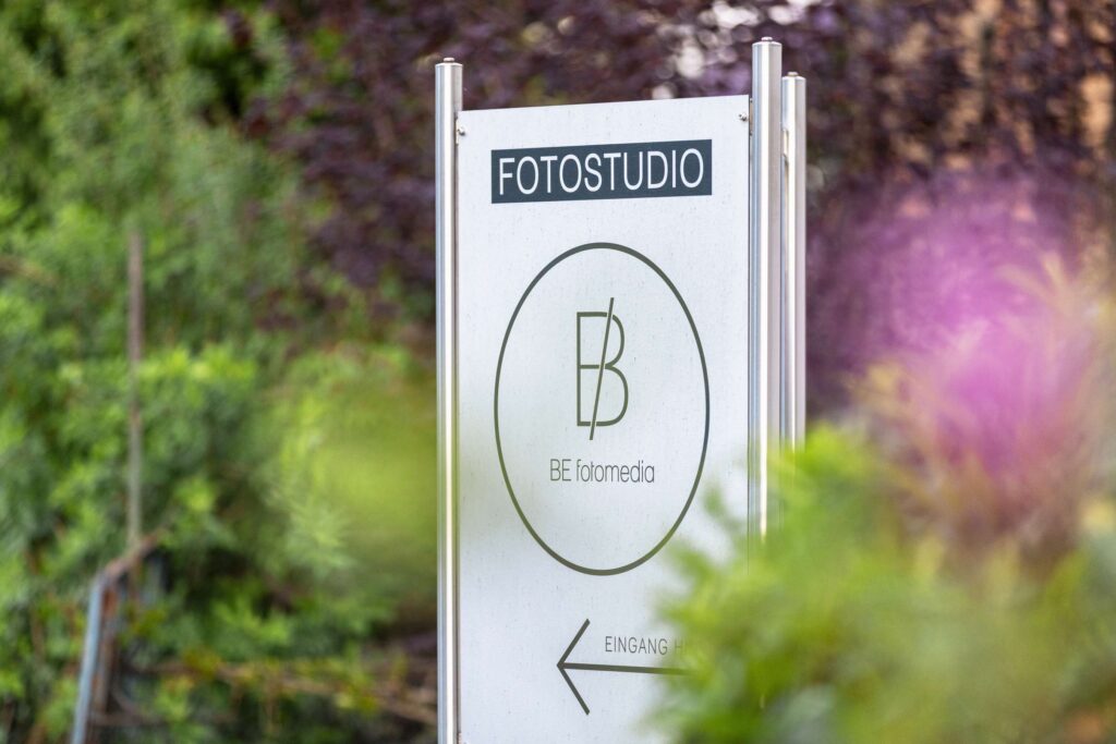 Hinweisschild mit Befotomedia-Logo und Wegweiser zum Fotostudio umgeben von gruener Natur