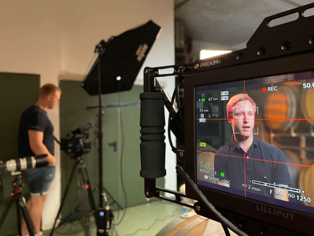 Alt-Text: Eine Behind-the-Scenes-Aufnahme einer Videoproduktion mit einer Person auf einem Bildschirm und einem Kameramann im Hintergrund.