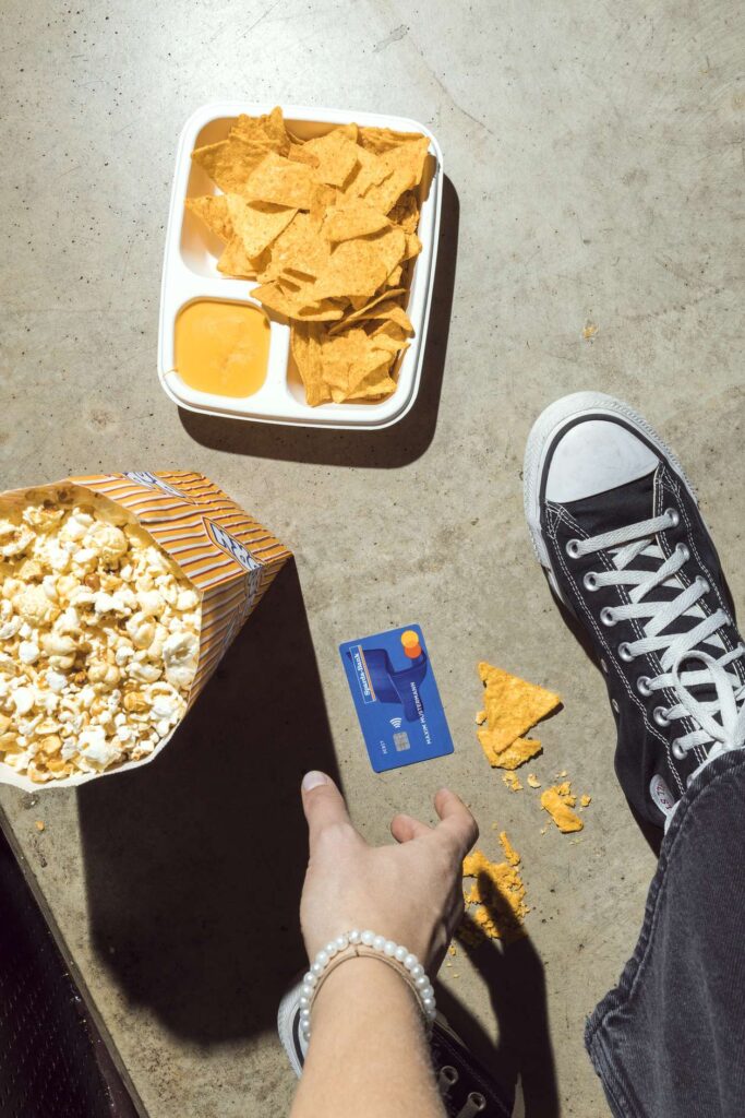 Eine Person mit Turnschuhen steht auf einem Boden mit Popcorn, Nachos und einer blauen Karte.