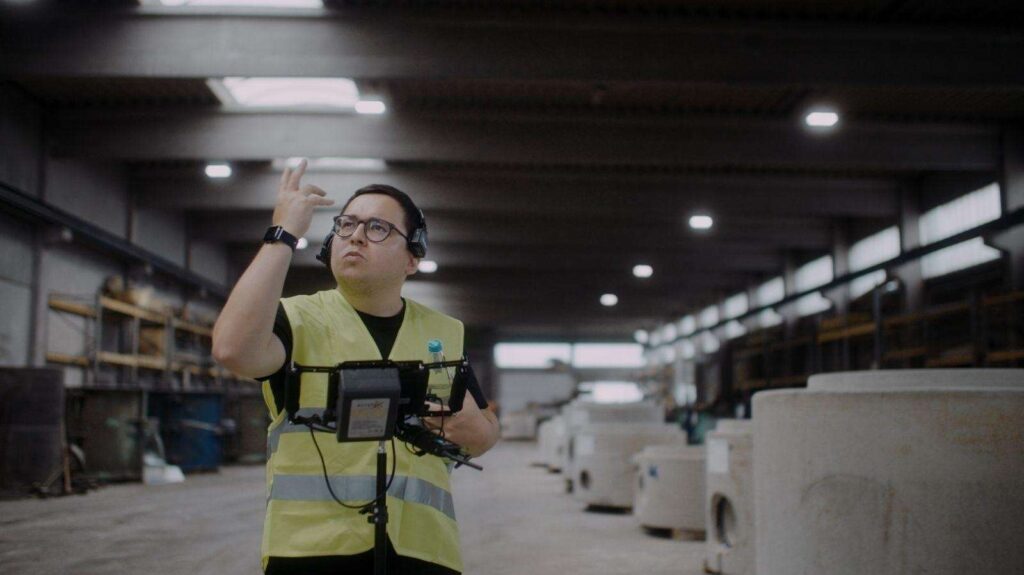 Ein Fotograf in einer Lagerhalle mit gelber Warnweste bei der Arbeit.