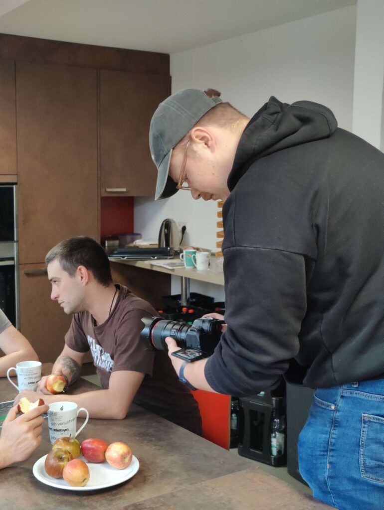 Ein Fotograf macht Aufnahmen von einer Person in einer Kueche mit Essen auf dem Tisch. oplus_1048624