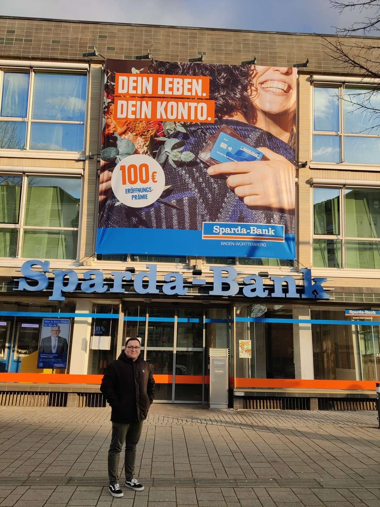 Person steht vor der Sparkasse mit großem Werbebanner an der Fassade