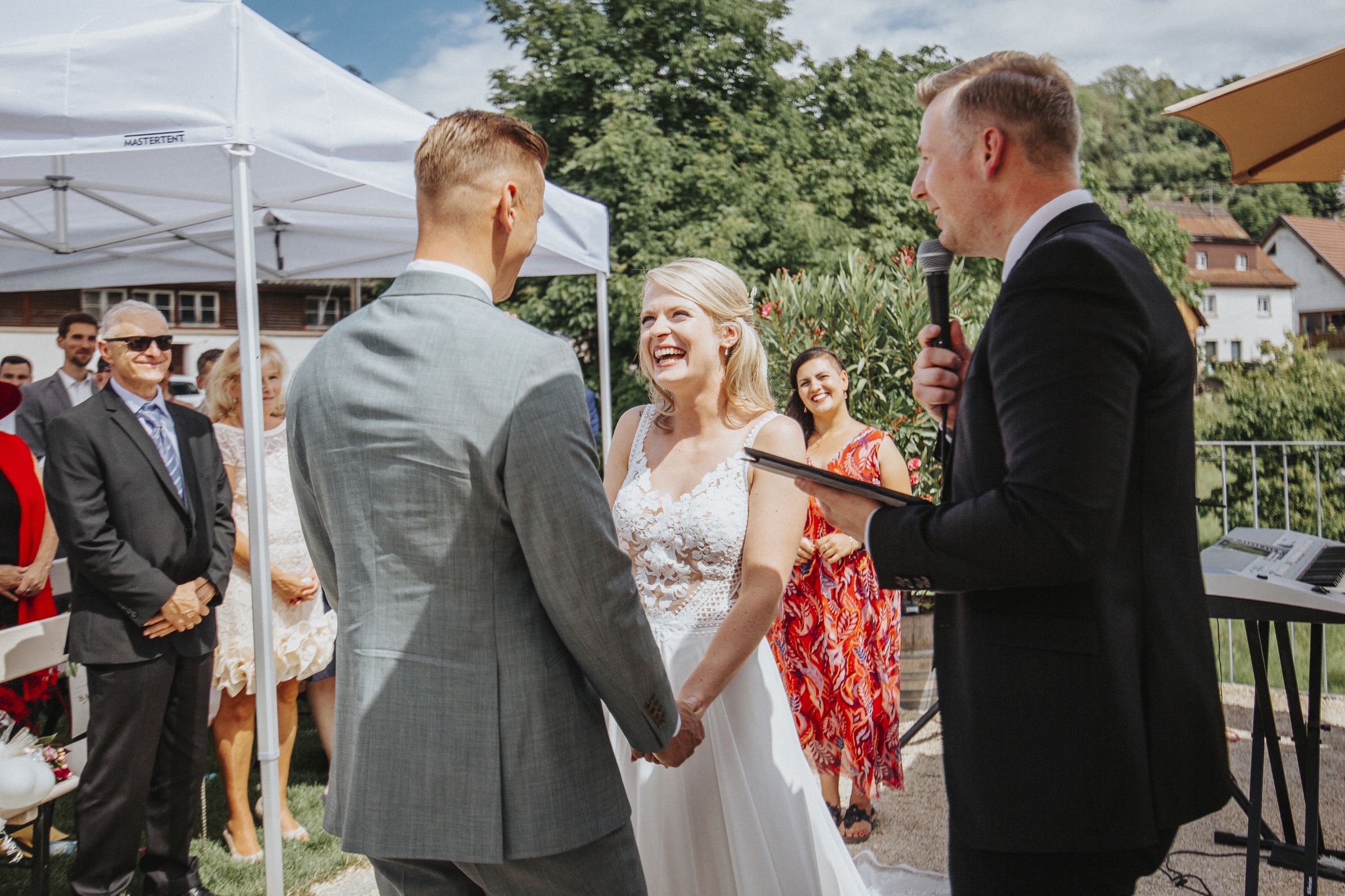 Brautpaar waehrend der Trauung im Freien mit Gaesten im Hintergrund