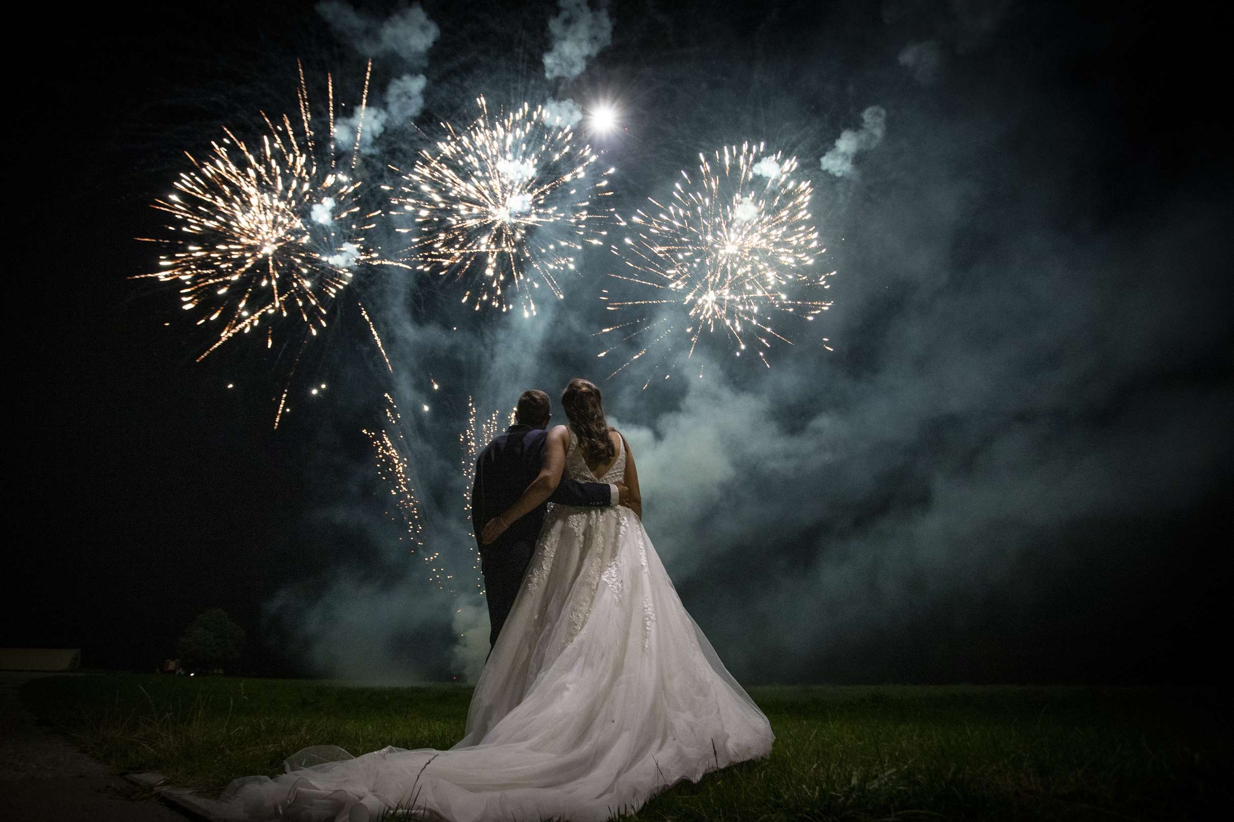 Ein Brautpaar steht unter einem naechtlichen Feuerwerk.