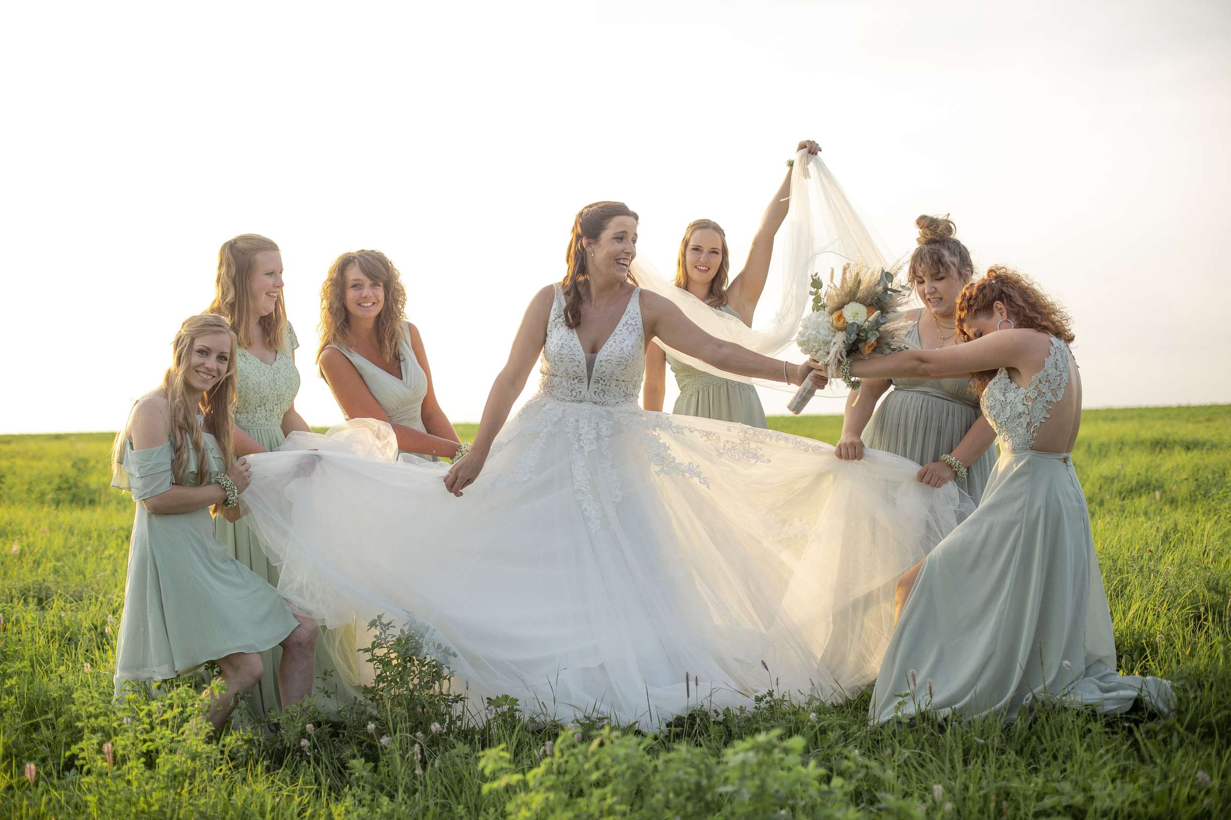 Eine Braut mit fuenf Freundinnen in einem Feld waehrend eines Hochzeitsfotoshootings.