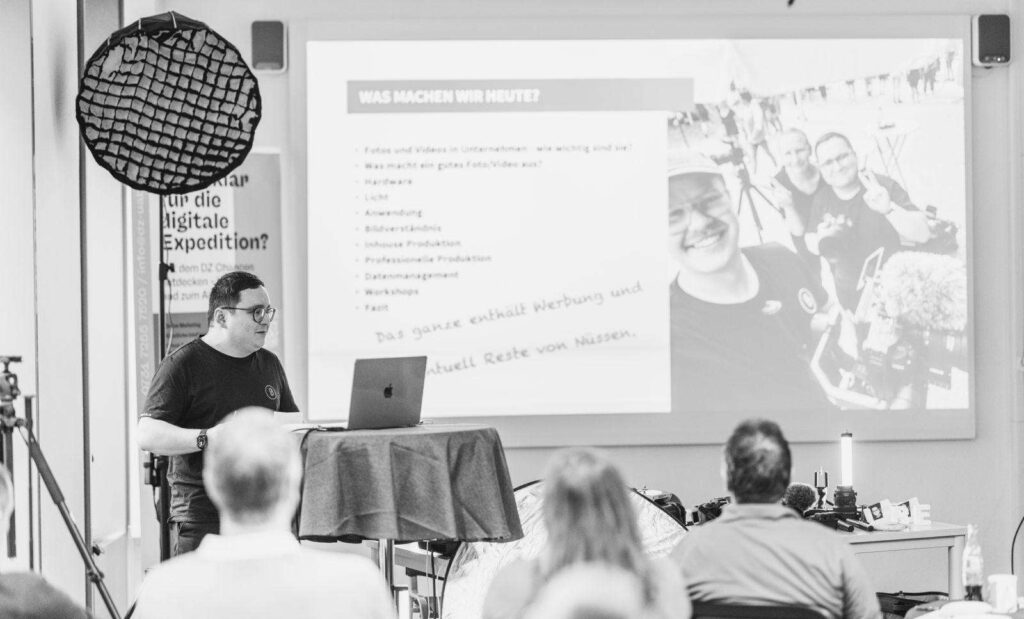 Person haelt eine Praesentation vor Publikum in einem Konferenzraum