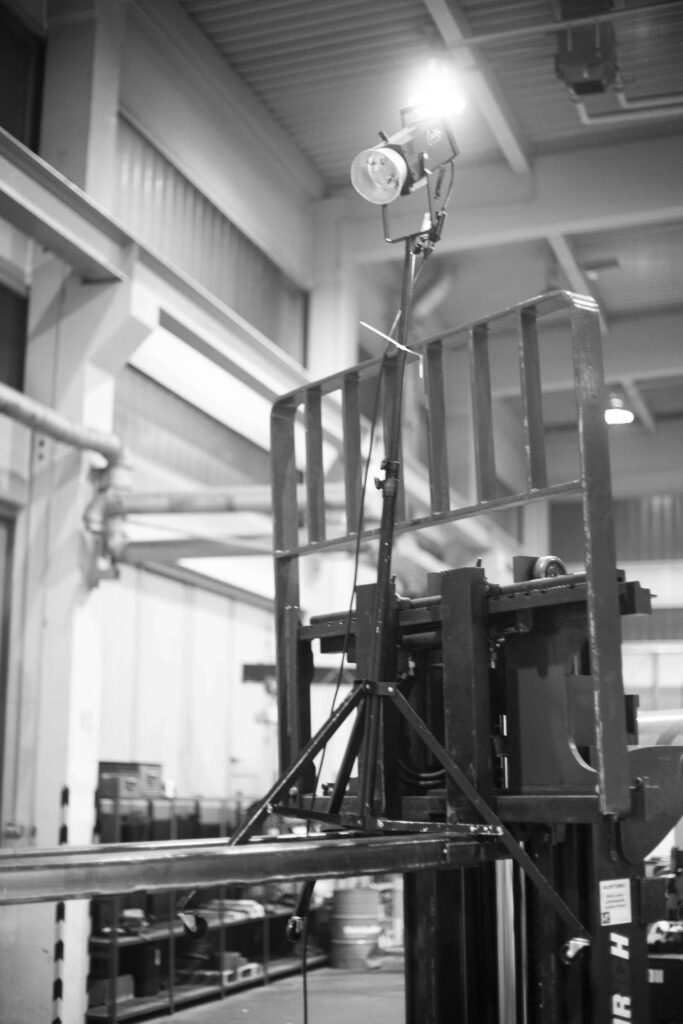 Alt-Text: Schwarz-weiß Bild eines Fotostudios mit professioneller Beleuchtungsausruestung und Kamera auf einem Hochstativ.