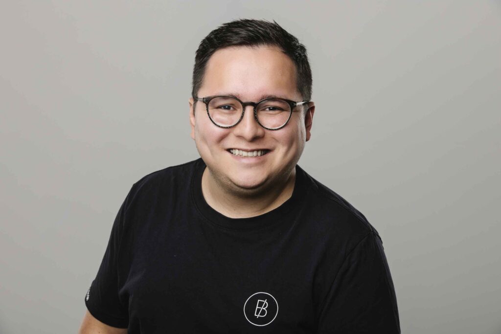 Ein Mann mit schwarzem Shirt und Brille laechelt in die Kamera.