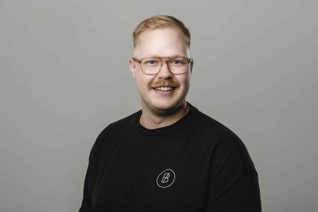 Ein Mann mit schwarzem Shirt und Brille laechelt in die Kamera.