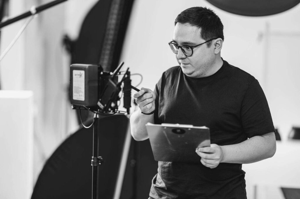 Eine Person steht vor einer Kamera und haelt ein Klemmbrett in einem Fotostudio.